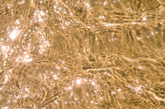 Ripple water of golden color with sandy bottom. Transparent sea water surface with sunny glares pattern and gritty bottom.