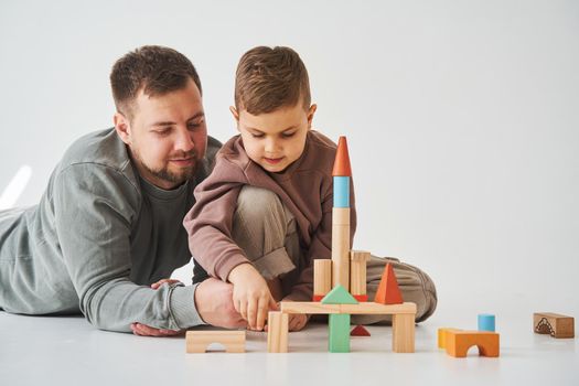 Paternity. Son and dad playing with colored bricks toy on white background. Father takes care of his kid