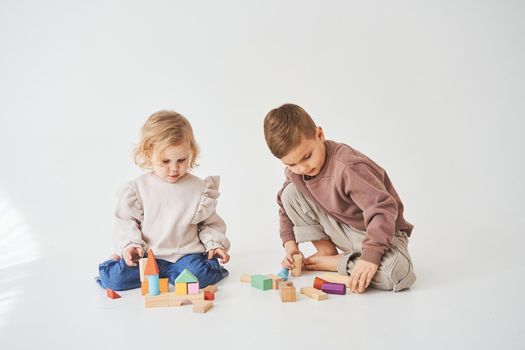 Child girl plays with cheerful kid with toy wooden cubes on white background. Children have smiling and have fun together