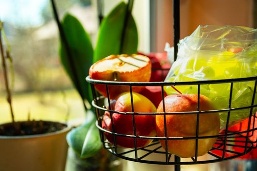 Apples and green grapes in a fruit basket in the kitchen, sunny day