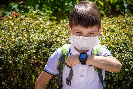 Photo of the boy looking at a smart watch. Children and modern technology. Coronavirus school reopening concept. Covid-19, health, education, safety, and back to school.