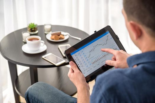 Man trading digital currencies online while relaxing by the cup of coffee in expencive hotel room.