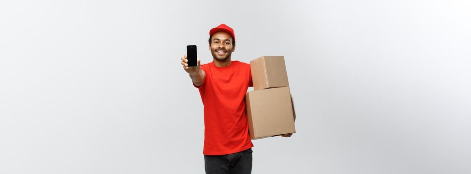 Delivery Concept - Portrait of Handsome African American delivery man or courier with box showing mobile phone on you to check the order. Isolated on Grey studio Background. Copy Space