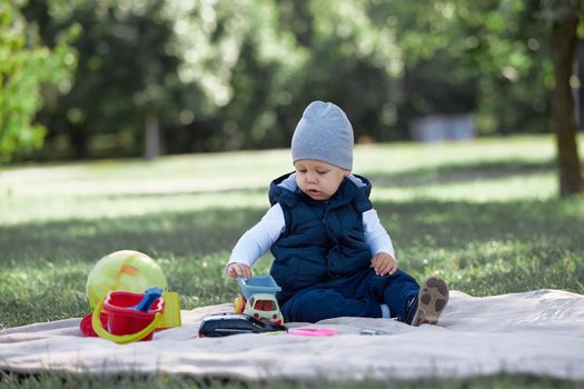 pretty little boy playing with a toy car sitting on the lawn in the Park