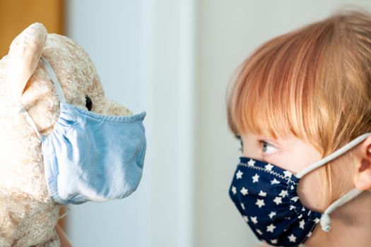 Young girl training to use a face mask during the pandemic -Focus on the teddy.