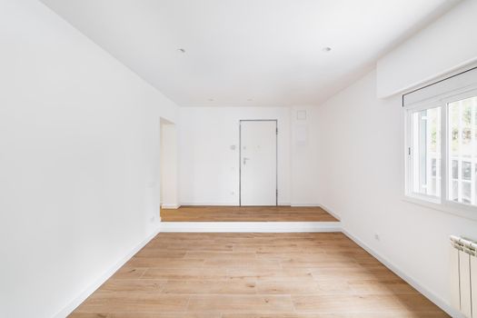 Empty room after renovation with window, white walls and wooden floor in new apartment.