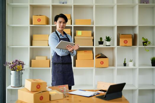 Startup small business SME, Entrepreneur owner using laptop computer taking receive and checking online purchase shopping order to preparing pack product box. Selling online ideas concept.