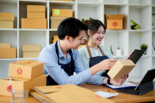 startup small business owner working with tablet at workplace. freelance man and woman seller check product order, packing goods for delivery to customer. Online selling, e-commerce, shipping concept.