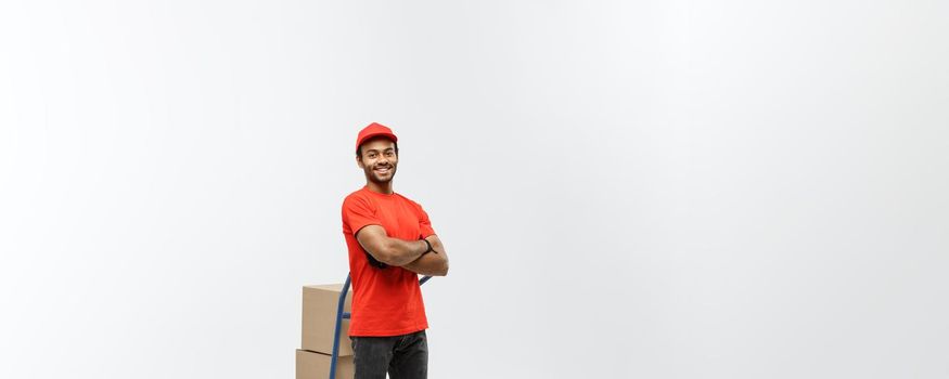 Delivery Concept - Portrait of Handsome African American delivery man or courier pushing hand truck with stack of boxes. Isolated on Grey studio Background. Copy Space