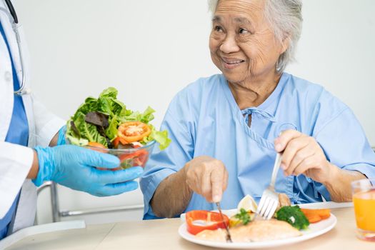 Asian senior or elderly old lady woman patient eating breakfast vegetable healthy food with hope and happy while sitting and hungry on bed in hospital.