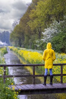 Young woman with yellow raincoat and rubber boots in spring nature