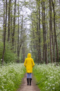 Young woman with yellow raincoat and rubber boots in spring nature