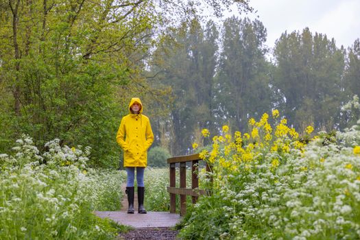 Young woman with yellow raincoat and rubber boots in spring nature