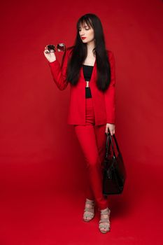 Portrait of young beautiful woman thoughtfully looking down. Brunette model in elegant costume posing at camera . Pretty lady in red sunglasses leaning one hand on other and holding it near face.