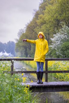 Young woman with yellow raincoat and rubber boots in spring nature