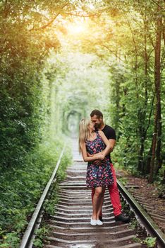 Loving couple in a tunnel of green trees on railroad.