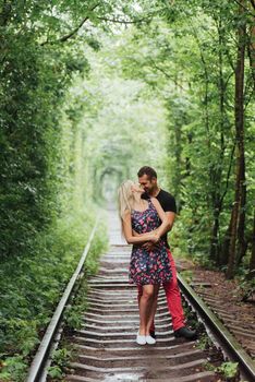 Loving couple in a tunnel of green trees on railroad.