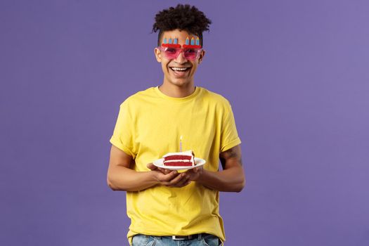 Celebration, party and holidays concept. Portrait of upbeat, charismatic lively man with dreads, hipster guy wearing funny glasses mask celebrating birthday, have fun, hold cake with candle.