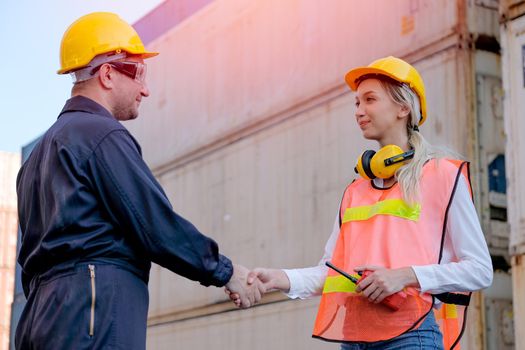 Technician man and woman shake hand together in front of cargo container with concept of successful in shipping business.