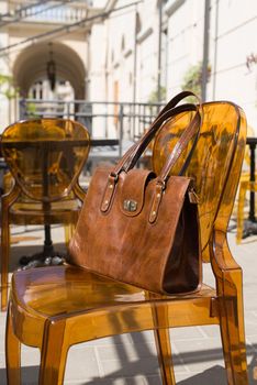 close-up photo of yellow leather bag on a stylish plastic chair. Outdoor photo