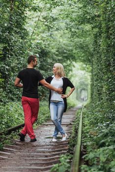 Loving couple in a tunnel of green trees on railroad.