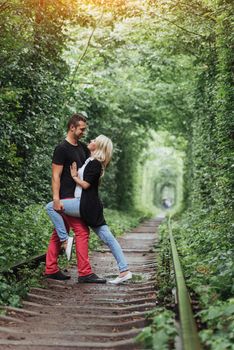 Loving couple in a tunnel of green trees on railroad.