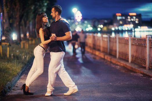 young couple dancing tango on the embankment of the river in the evening