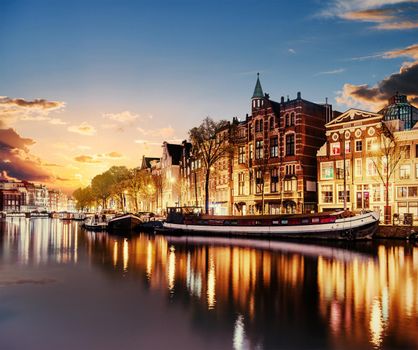 Beautiful night in Amsterdam. Night illumination of buildings and boats near the water in the canal.