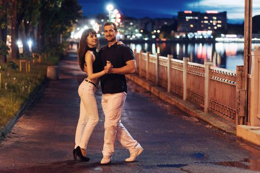 young couple dancing tango on the embankment of the river in the evening