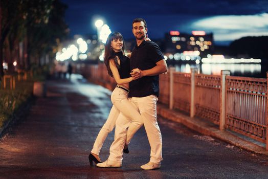 young couple dancing tango on the embankment of the river in the evening