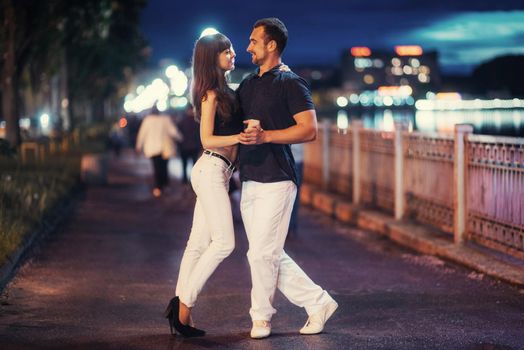young couple dancing tango on the embankment of the river in the evening