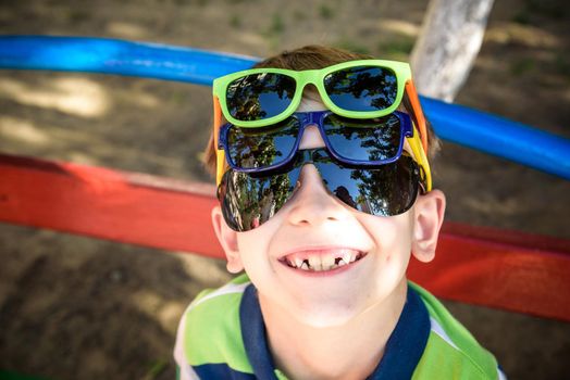 Portrait of a cheerful boy child in several sunglasses outdoors. Beauty, summer casual fashion. Optics for children. Sun protection.