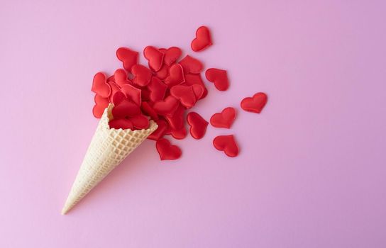 Sweet waffle cone on a pink background with red hearts. Place for your text.