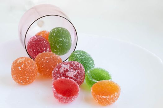 A pile of red, green and yellow jelly cubes on a white plate on a white background