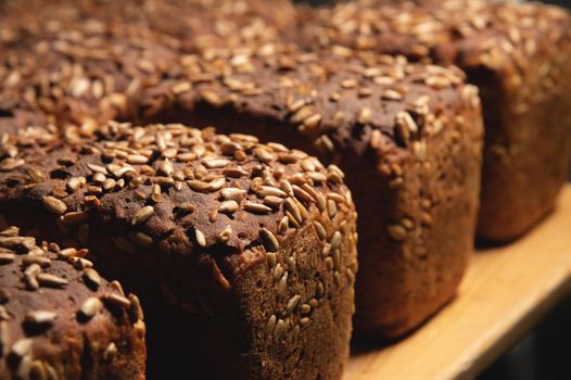 Close-up rye loaves of hot rye bread stand on a wooden tray in a dark bakery room.