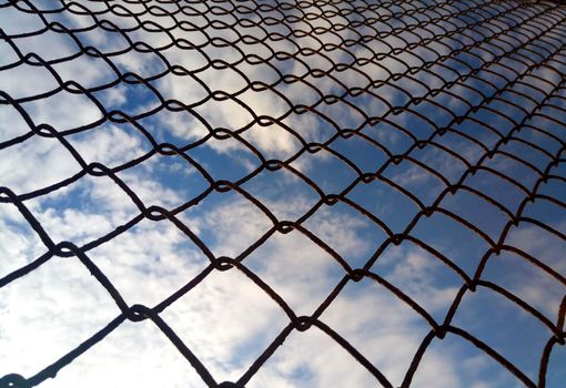 Bright blue sky with white clouds through a metal grid chain fence. Mesh background.