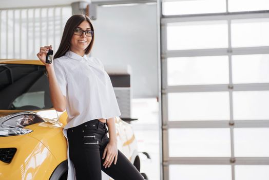 Portrait of a young beautiful woman looking at the camera at the car showing keys.