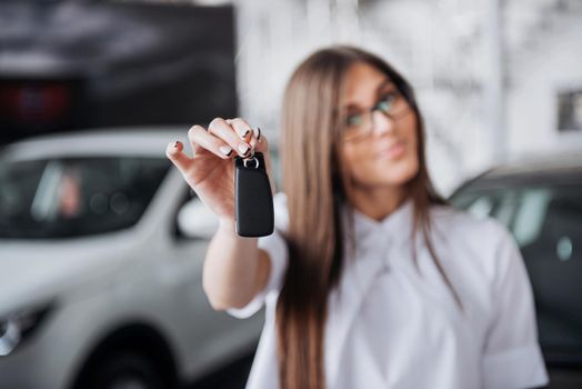 Portrait of a young beautiful woman looking at the camera at the car showing keys.