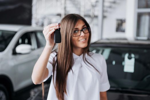 Portrait of a young beautiful woman looking at the camera at the car showing keys.