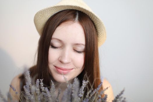 Beautiful young woman wearing summer hat and holding lavender flowers