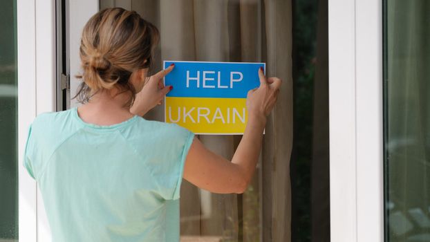 Woman sticking sign on door help Ukraine closeup. Charitable assistance for Ukrainian people concept