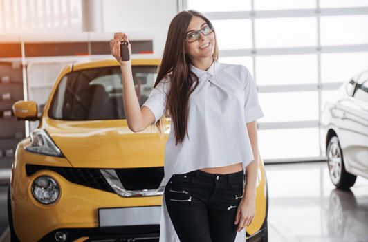 Portrait of a young beautiful woman looking at the camera at the car showing keys.