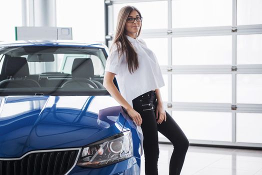 Pretty girl is standing near her car. She is leaning on the roof and is looking aside dreamingly. She is smiling with anticipation