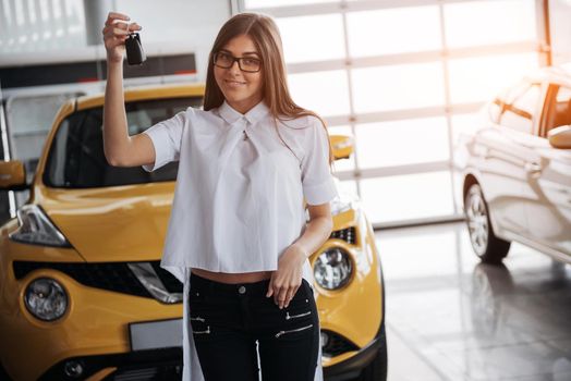 Portrait of a young beautiful woman looking at the camera at the car showing keys.