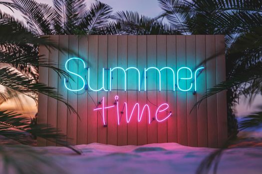 3D rendering of Summer Time bright neon signboard on wooden fence placed on sandy beach with lush palm trees under cloudless sunset sky