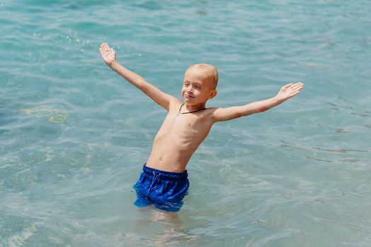 Child learning to swim in the open sea of tropical resort. Kids learn swimming. Exercise and training for young children. Little boy with colorful float board in sport club. Swimming baby or toddler. Happy child boy swims in sea in swimming circle with splash. Blue sky and water. Swimming training. Fun joy activities on vacation in the beach. Childhood moments lifestyle. Freedom careless. boy swim in the sea.