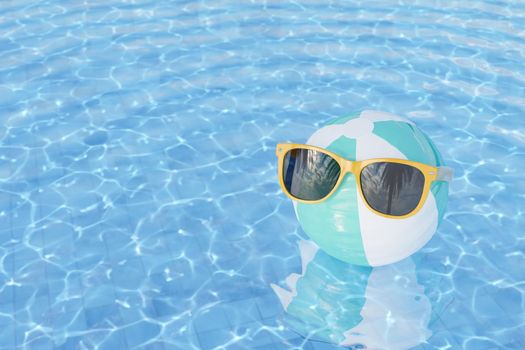 3D rendering of trendy yellow sunglasses on striped inflatable beach ball floating in rippling water of outdoor swimming pool on summer day