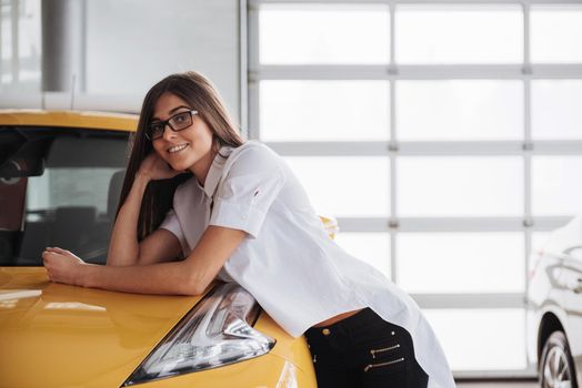 Pretty girl is standing near her car. She is leaning on the roof and is looking aside dreamingly. She is smiling with anticipation
