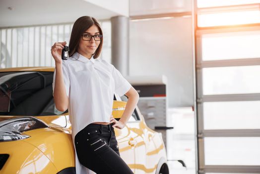 Portrait of a young beautiful woman looking at the camera at the car showing keys.