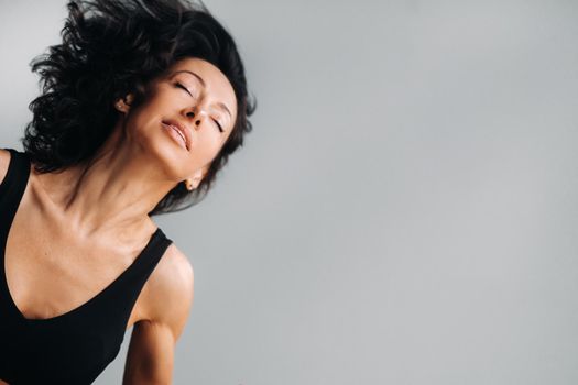 A woman in a black sports T-shirt waves her head with her long hair loose on a gray background.